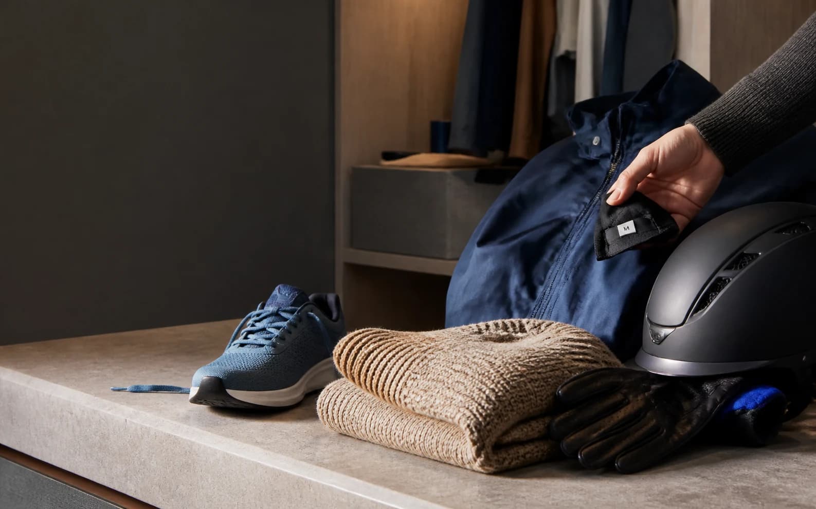 Clothing, a running shoe, helmet, and gloves arranged while a hand checks a garment size tag