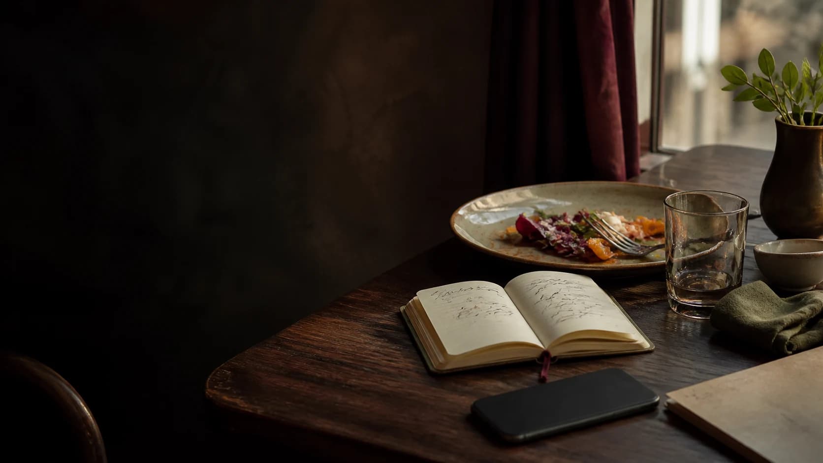 A quiet restaurant table with an open food journal, a finished plate, and a phone